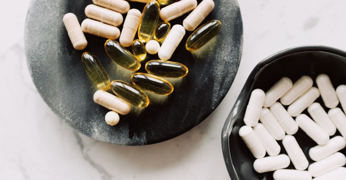 Top view of biologically active additives include tablets and capsules placed in ceramic bowl and on stone stand against marble board