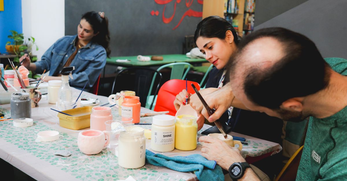 Three adults engaged in a vibrant pottery class, painting ceramic pieces with colorful glazes.